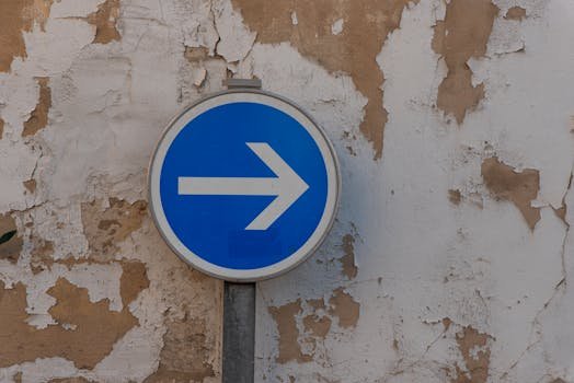A blue and white traffic sign with an arrow against a weathered wall.