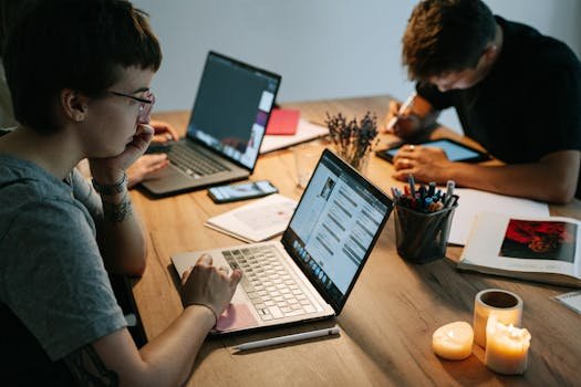 Two young professionals collaborating in a cozy office with laptops, notebooks, and candles.