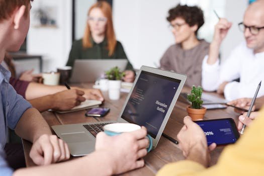 A diverse group of professionals collaborating with laptops and tablets in a modern office setting.