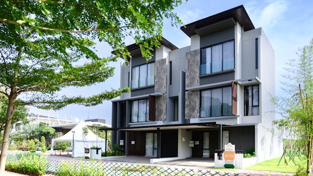 Contemporary three-story residential building set amidst lush green landscape on a clear day.