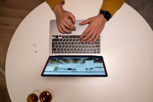 Person typing on a laptop with yellow sleeves visible, aerial perspective.