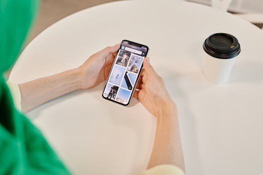 Close-up of hands holding smartphone browsing images with coffee cup on table.