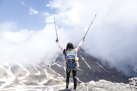 Woman with backpack celebrating reaching a mountain summit with raised hiking poles.