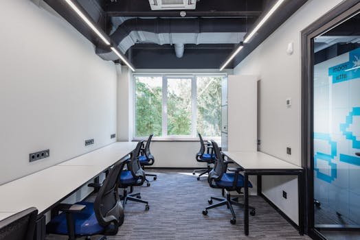 Contemporary open space office with white tables and armchairs placed near glass door and big window in creative business center