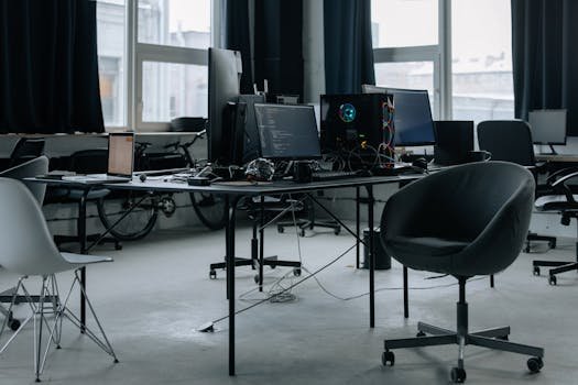 Discover a modern office workspace with computers, chairs, and natural light from large windows.