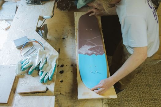 A man intricately working on a skateboard design in a woodcraft workshop, showcasing craftsmanship.
