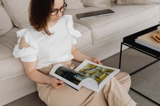 Woman in comfortable living room reading a magazine on the sofa, wearing casual chic attire.