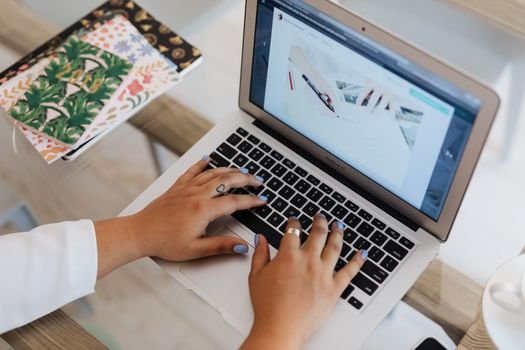 Close-up of hands typing on a laptop at a stylish office desk with notebooks.