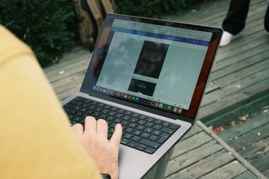 Person typing on a laptop outdoors on a wooden deck. Perfect for work-from-anywhere concepts.