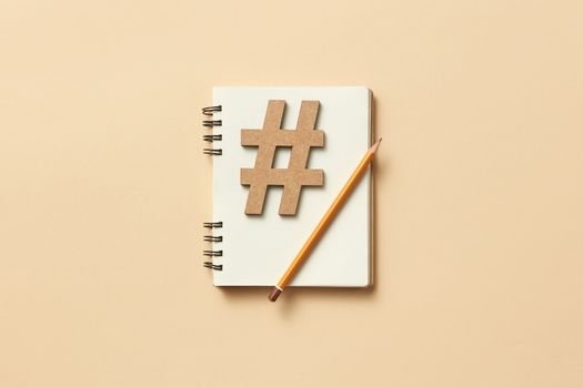 Minimalist flat lay featuring a notebook, hashtag symbol, and pencil on beige background.