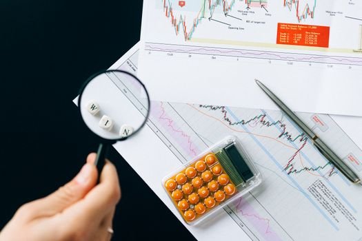 Magnifying glass highlighting the word 'WIN' over financial charts. Enhance your business analysis vision.