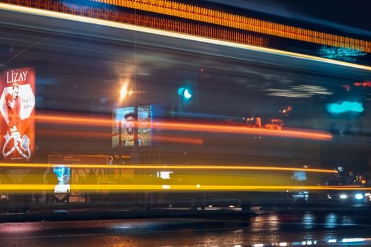 A vibrant city street at night with motion blur and colorful light trails from vehicles.