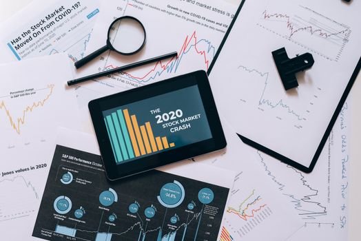 Tablet displaying 2020 stock market crash amidst graphs and charts. Perfect for financial analysis themes.