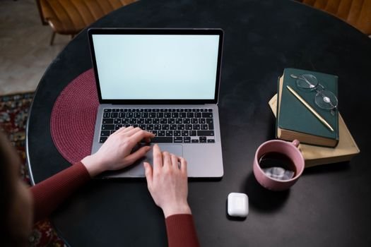Hands typing on a laptop at a stylish indoor workspace with coffee and books.