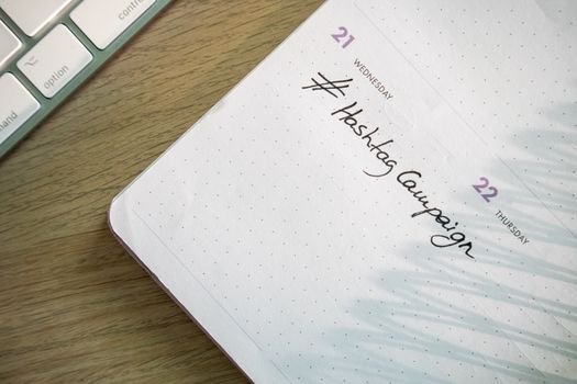 Open planner with 'Hashtag Campaign' handwritten next to keyboard. Ideal for social media and productivity themes.